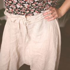 a woman in floral shirt and white pants with her hands on her hips, looking at the camera