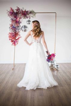 a woman in a wedding dress standing next to a floral arch with flowers on it