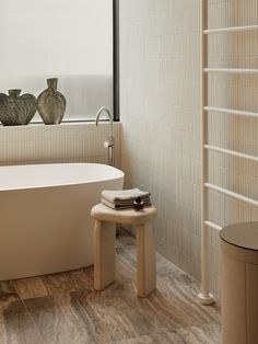 a white bath tub sitting under a window next to a wooden table with two vases on it