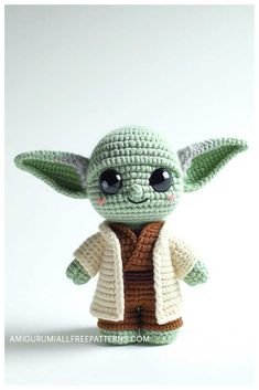 a crocheted baby yoda doll is posed in front of a white background