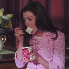 a woman in pink jacket eating food off of a cup with flowers on top of it