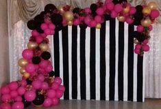 a black and white striped backdrop with pink and gold balloons on the floor, along with some other decorations