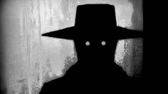 the silhouette of a man wearing a hat with two white eyes in front of a grungy wall