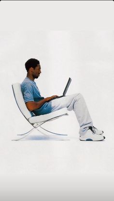 a man sitting in a white chair with his laptop on his lap and looking at the screen