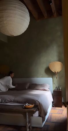 a person laying on a bed in a room with green walls and ceiling lights hanging from the ceiling