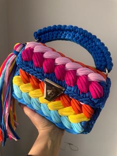 a hand holding a multicolored purse with tassels on the front and side