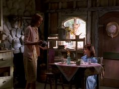 two women standing in a kitchen next to a table and chairs with dishes on it