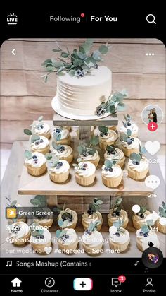 a cake and cupcakes are arranged on a wooden stand with greenery around it