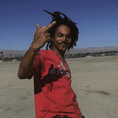 a man with dreadlocks standing in the middle of an empty field holding his hand up