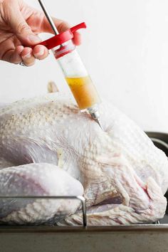 a person holding a syil over a turkey on a pan with an orange substance in it