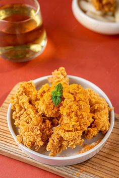 fried food in a white bowl on a wooden tray next to a glass of tea