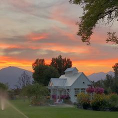 a white house with a sprinkler in the foreground and mountains in the background