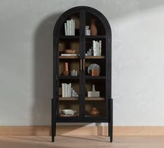 a black bookcase with many books and vases on it in front of a white wall