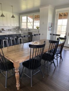 a dining room table with black chairs and an island in the middle is surrounded by white cabinets