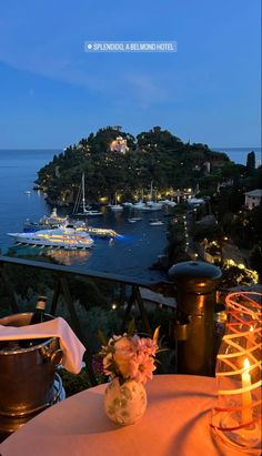 a table with flowers and candles on it overlooking the water at night, in front of boats