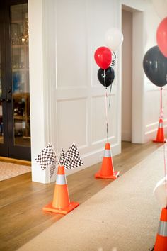 some orange and black traffic cones are on the floor with balloons in the air behind them