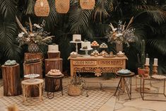 a table topped with lots of cakes and desserts next to tall palm trees in the background