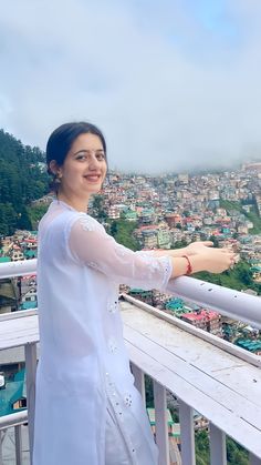 a woman standing on top of a balcony next to a lush green hillside filled with houses