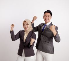 two people dressed in business attire posing for the camera with their fists up and one person wearing a headscarf