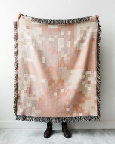 a person standing in front of a white wall holding a pink and beige blanket with fringes