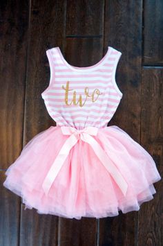 a pink and white striped tutu dress with gold lettering on the chest, sitting on a wooden floor