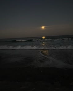 the moon is setting over the ocean with waves