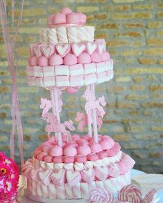 a pink and white cake with lots of candy on it's stand next to flowers