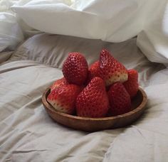 a wooden bowl filled with strawberries on top of a bed