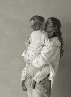 a woman holding a child in her arms and kissing the baby's face with both hands