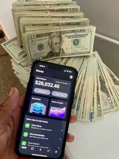 a person holding a cell phone in front of stacks of money