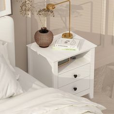 a white nightstand with a book and vase on it next to a bed in a bedroom