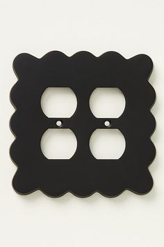 a black double outlet cover on a white wall with two holes in the middle and one hole at the bottom