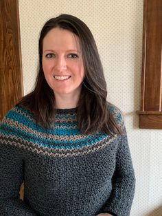 a woman standing in front of a mirror wearing a blue and gray knitted sweater