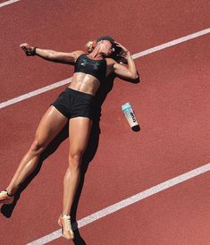 a woman laying on the side of a track next to a bottle of water and a drink