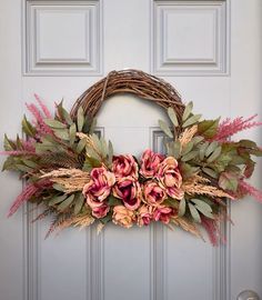 a wreath with pink flowers and green leaves hanging on a front door, next to a white door