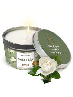 a candle that is sitting next to a flower and some tins with the words gardenia written on it