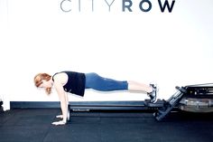 a woman is doing push ups on a stationary exercise machine in front of a city row sign