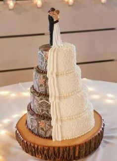 a wedding cake with a bride and groom topper sitting on a tree stump in front of string lights