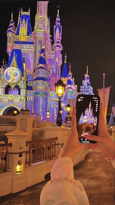 a person taking a photo with their cell phone in front of the castle at night