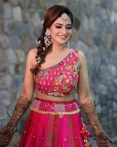 a woman in a pink lehenga and matching headpiece smiles at the camera