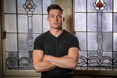 a man standing with his arms crossed in front of two stained glass windows behind him