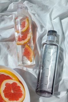 two grapefruits are next to a bottle of water on a white sheet