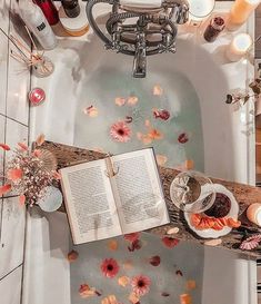 an open book sitting on top of a bathtub next to candles and flowers in the water