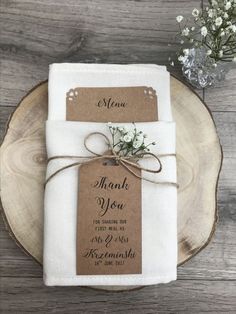 a wooden plate topped with a piece of paper next to a white napkin and flower