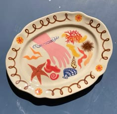 an oval shaped plate with hand painted designs on the rim and sides, sitting on a blue surface