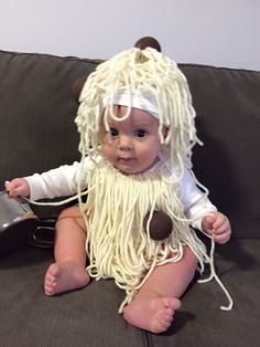 a baby sitting on a couch wearing a wig and holding a cell phone in it's hand