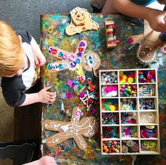 two children are playing with crafts on a table in front of a box full of beads