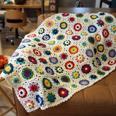 a crocheted granny blanket sitting on top of a brown leather chair in a living room