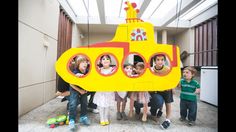 a group of children standing in front of a yellow submarine shaped cardboard boat with pictures on it