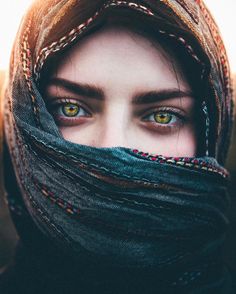 a woman with yellow eyes is wearing a scarf over her head and looking into the camera